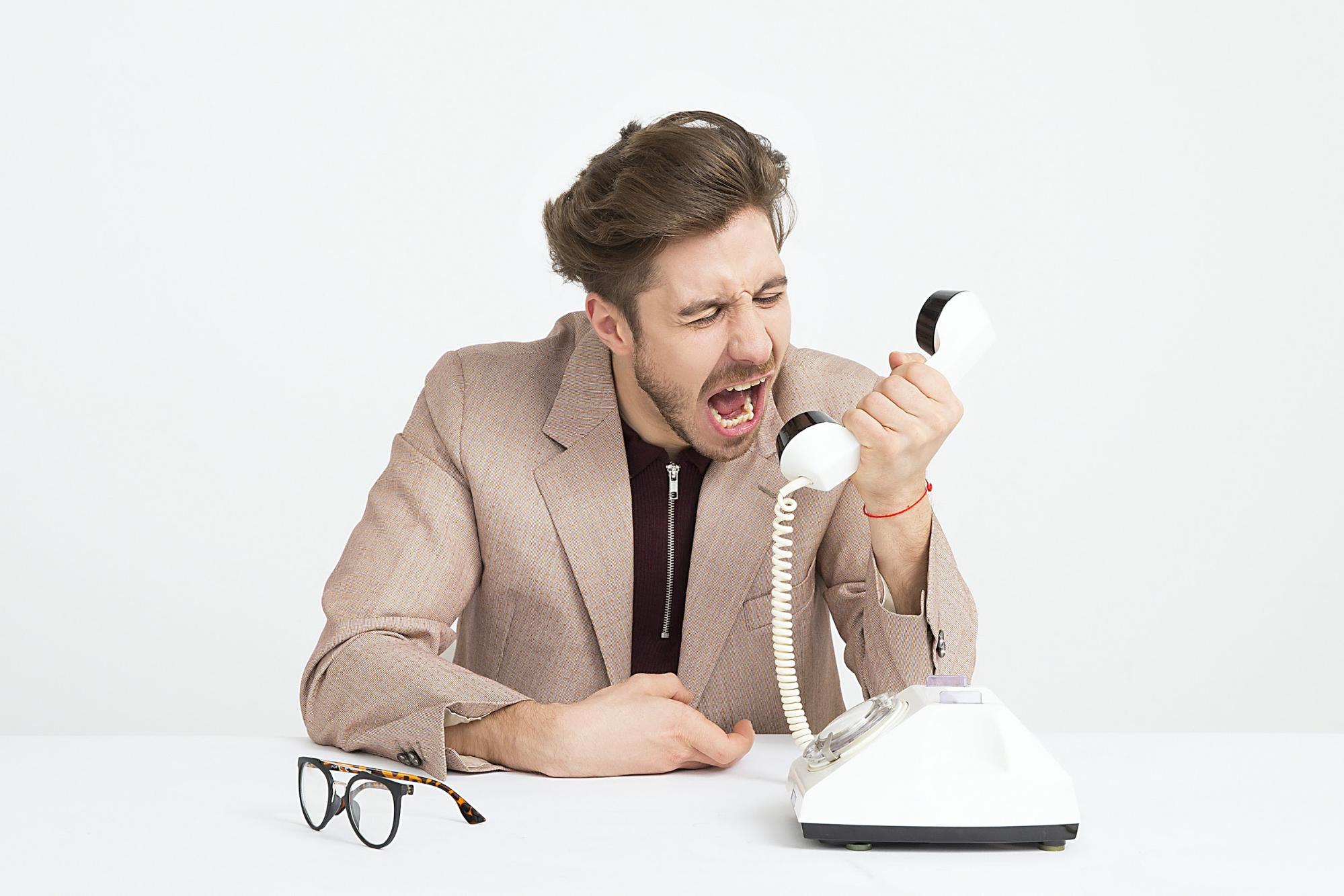 An angry young man is screaming into a telephone receiver 