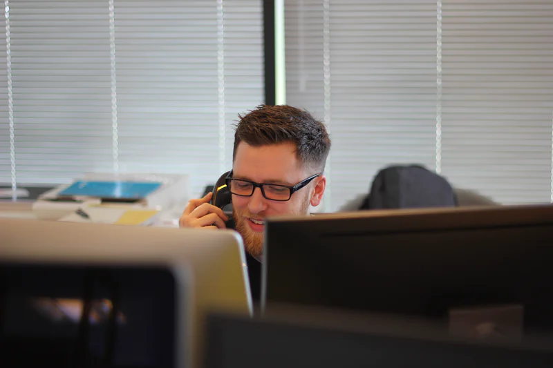 Young man in glasses is speaking on a phone in the office